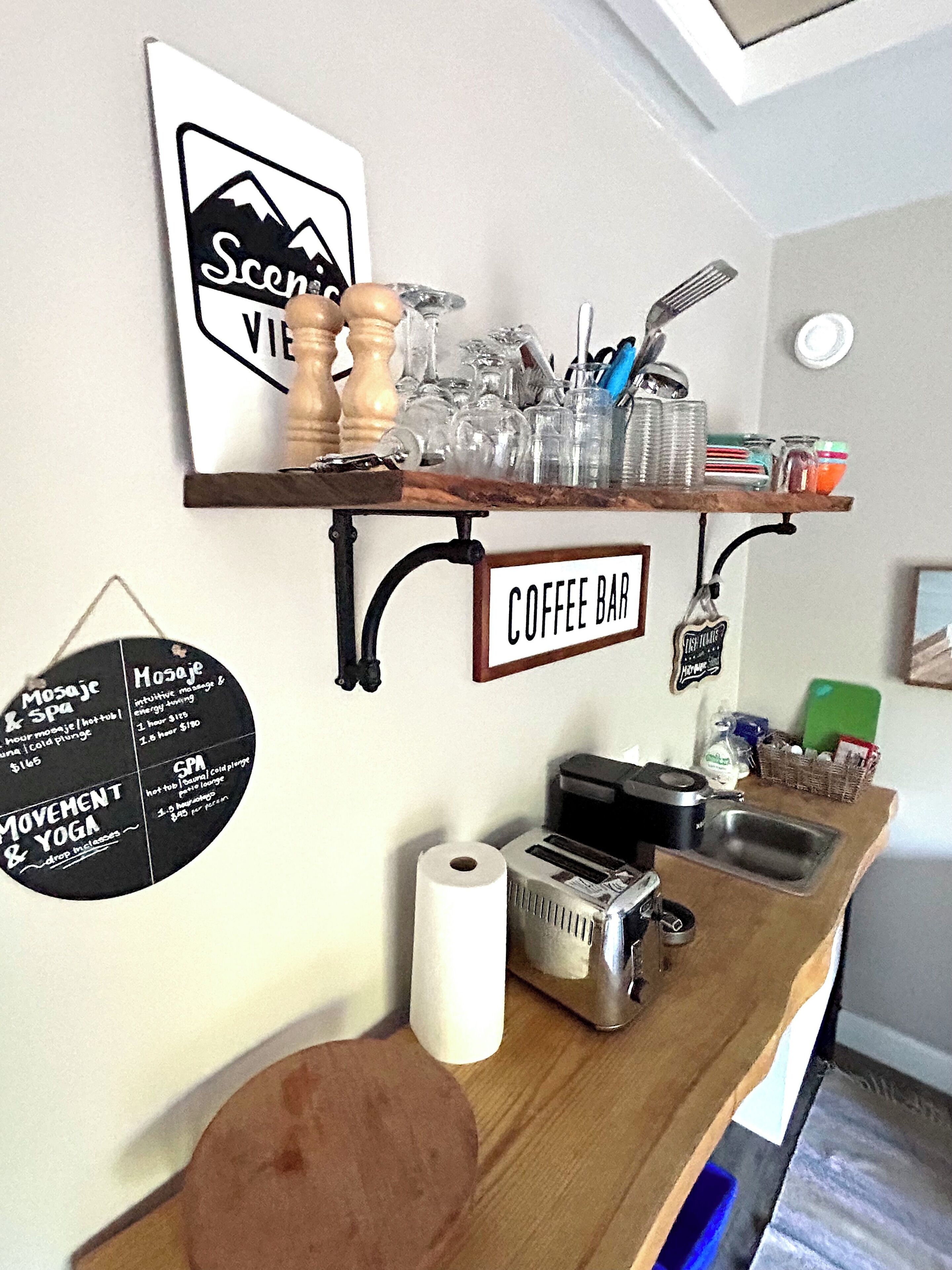 Un área de cafetería con un cartel que indica que es un café, un cartel para un spa y un cartel para movimiento y yoga. Hay varios objetos en la barra, como un tostador, un lavamanos y un rollo de papel de cocina.