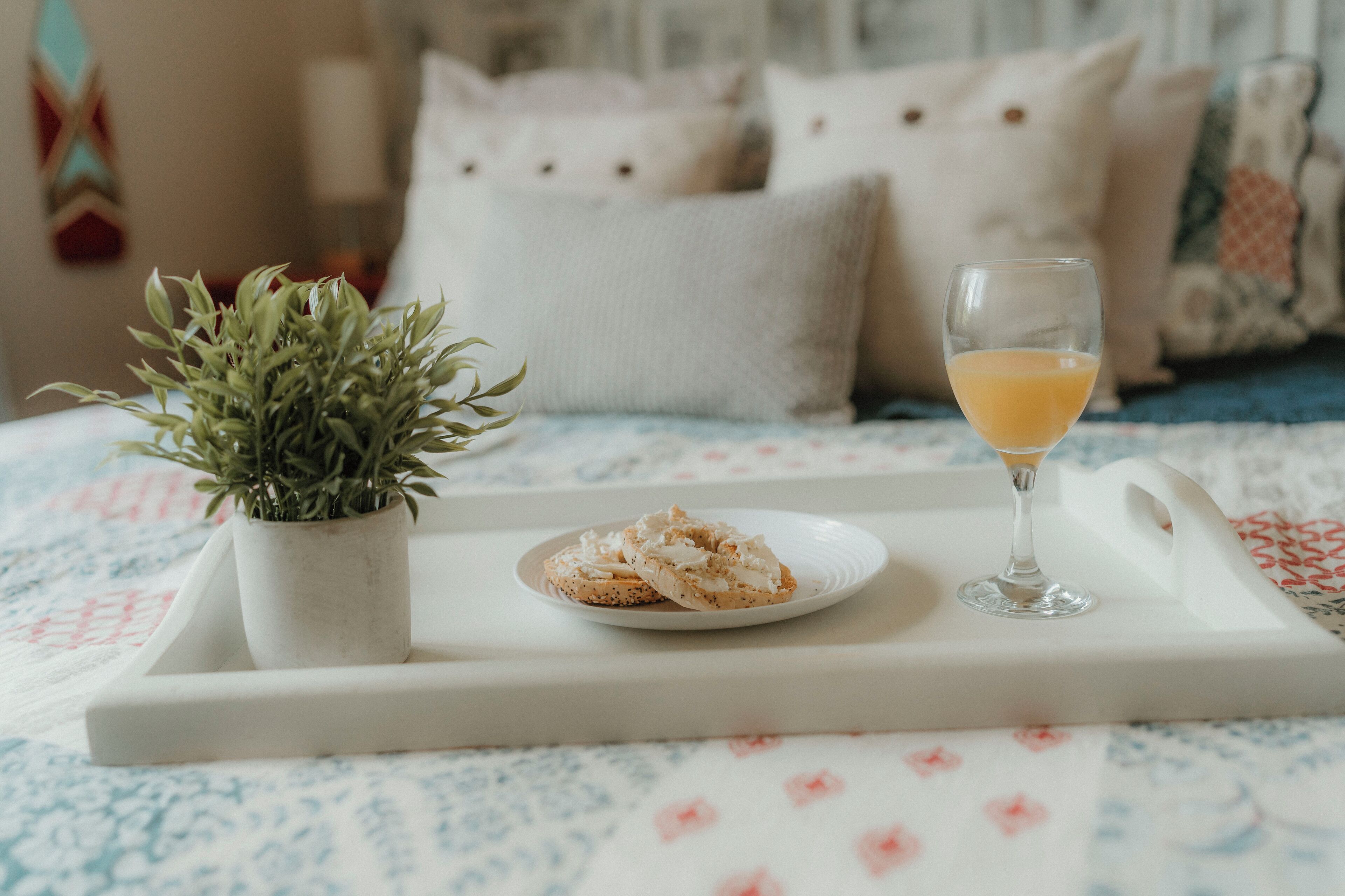 Una bandeja con pasteles y un vaso de jugo de naranja sobre una cama con colcha estampada de flores.