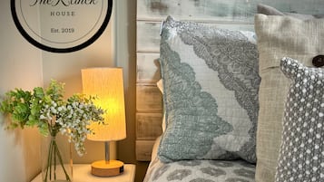 Un dormitorio ordenado con cama, almohadas, una mesita de noche con lámpara y un cartel en la pared.