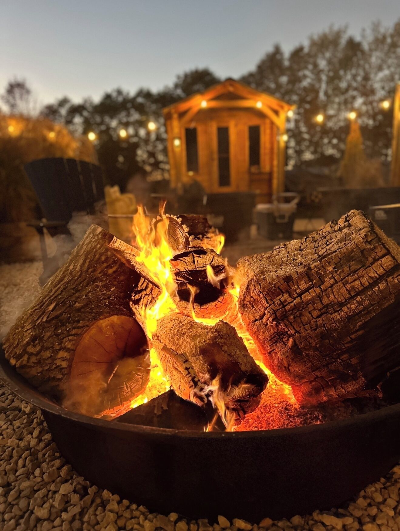 A campfire with logs and flames, surrounded by gravel.