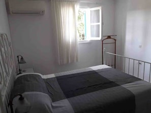 Une chambre à coucher avec un lit, une table de chevet, une lampe, une fenêtre avec des rideaux et un radiateur.