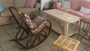 A living room with a beige sofa, a patterned rocking chair, a wooden coffee table, and a woven ceiling light fixture. - Apartment 'Cozy  For Rent In Kythera' with Shared Terrace, Wi-Fi and Air Conditioning (Κύθηρα)