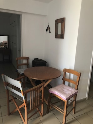 Un coin repas avec une table ronde et quatre chaises en bois, une petite poubelle noire et un miroir fixé au mur.