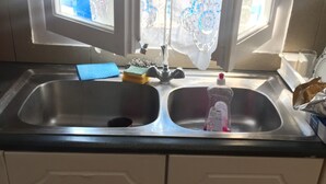 A kitchen with a double sink, a window with lace curtains, and a bottle of dish soap on the counter. - Apartment 'Cozy  For Rent In Kythera' with Shared Terrace, Wi-Fi and Air Conditioning (Κύθηρα)