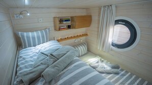 Habitación pequeña con cama, una estantería con libros, una ventana y una lámpara fijada a la pared.