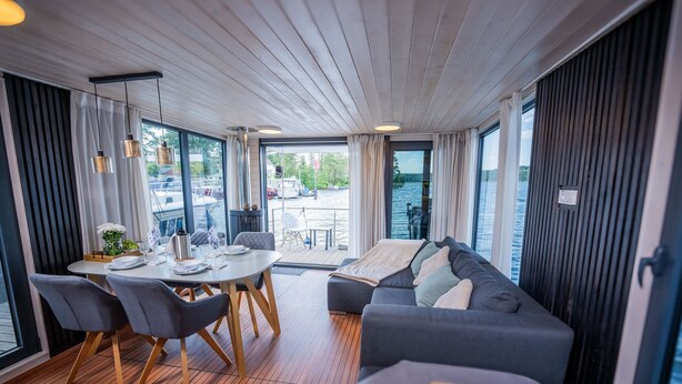 Un intérieur moderne comprenant un coin repas, un canapé et de grandes fenêtres donnant sur un plan d’eau.