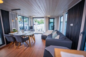 Ein modernes Interieur mit Essbereich, einer Couch und großen Fenstern mit Blick auf ein Gewässer.
