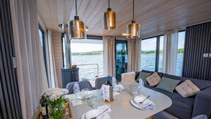 Un coin repas avec une table dressée pour quatre personnes, de grandes fenêtres et une vue sur une étendue d’eau.