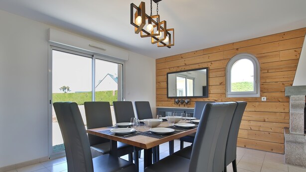 A dining area with a wooden wall, a large mirror, and a view of the outdoors. - Holiday Home "Gîte with Game Room" with Private Terrace, Garden & Wi-Fi (Montfarville)