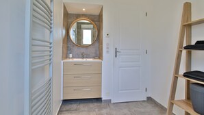 A modern bathroom with a white door, a round mirror, a beige vanity, and a towel rack. - Holiday Home "Gîte with Game Room" with Private Terrace, Garden & Wi-Fi (Montfarville)