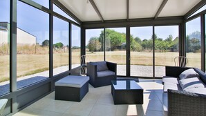 A sunlit patio with wicker furniture and a glass enclosure. - Holiday Home "Gîte with Game Room" with Private Terrace, Garden & Wi-Fi (Montfarville)