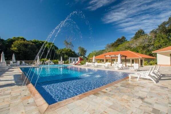 A swimming pool with a water fountain, lounge chairs, and a covered area with a red roof.