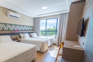 Ett hotellrum med två sängar, en TV och ett stort fönster med utsikt över grönområden.