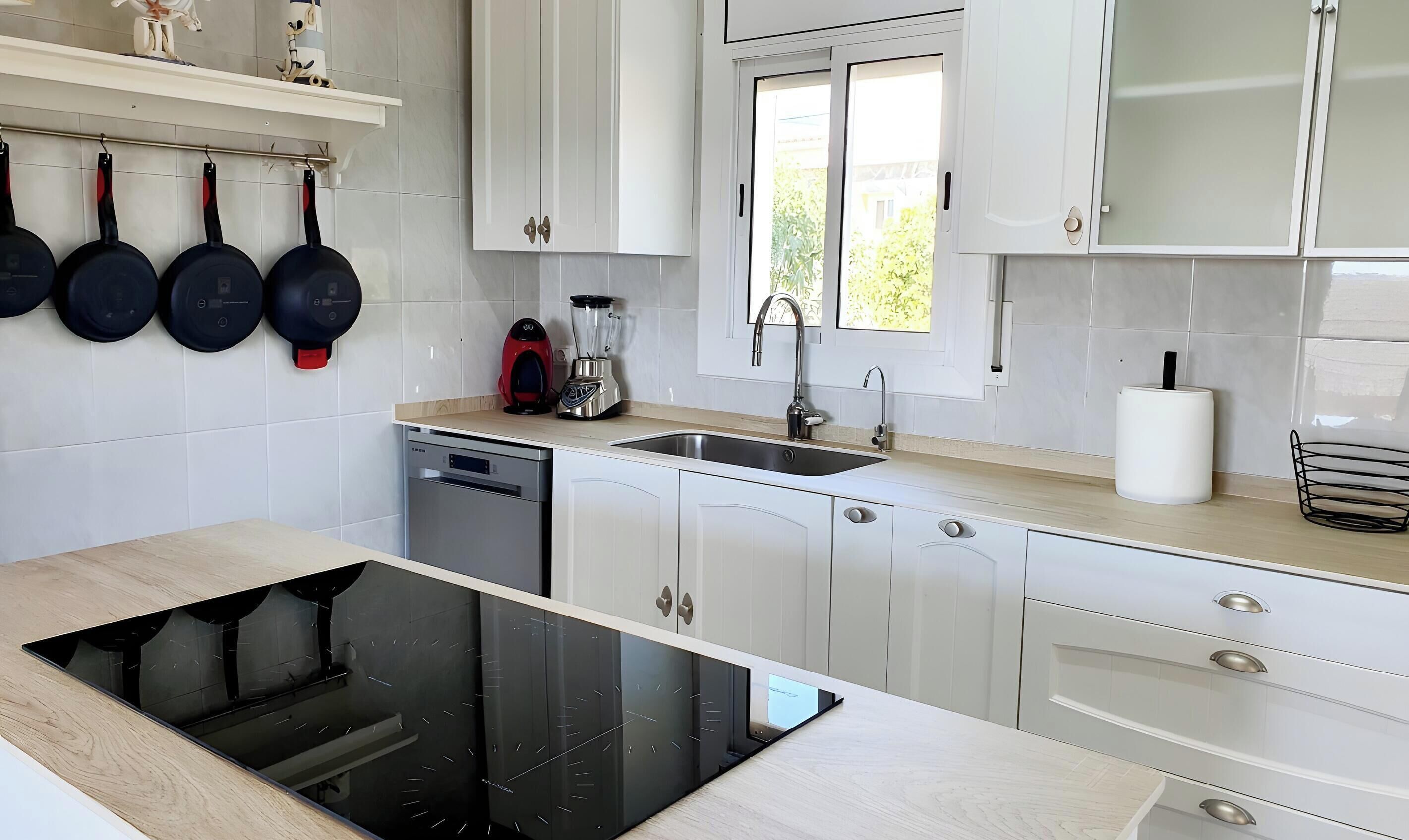 A modern kitchen with white cabinets, a dishwasher, a built-in oven, a sink, and a window.
