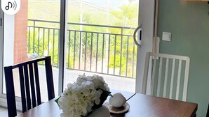 Een eethoek met een tafel, stoelen en uitzicht op een balkon met beplanting.