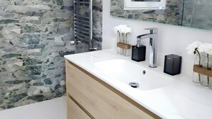 Een badkamer met een stenen muur, een witte wasbak, een spiegel en twee vazen met bloemen.