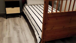 Een houten bed met een gestreept dekbedovertrek, een nachtkastje met een bloemenvaas, en een houten hoofdbord.