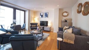 Ein modernes Wohnzimmer mit einer Couch, Sesseln, einem Couchtisch und einem Fernseher.