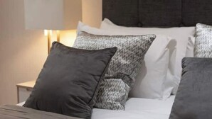 Ein ordentlich bezogenes Bett mit gemusterten Kissen und einer Nachttischlampe.