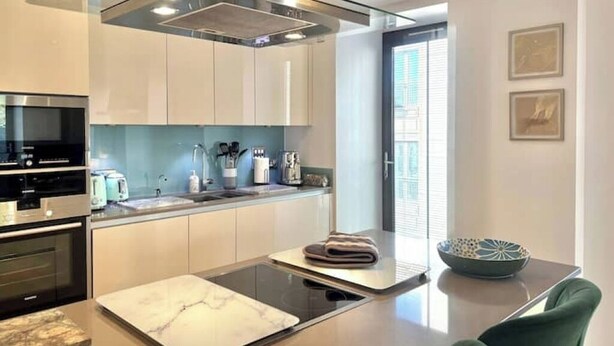 Una cocina moderna con horno integrado, microondas, placa de cocina y una isla grande con tabla de cortar.