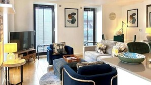Una sala de estar moderna con un televisor de pantalla plana, un sofá, una silla y una mesa de comedor con un bol.