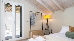 Un dormitorio con cama, lámpara de noche, aparador de madera y vistas a través de una puerta corredera.