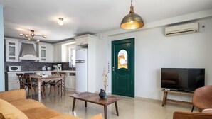 Una sala moderna con un sofá, una mesa de centro y un televisor. Se ve un comedor con sillas y una mesa al fondo.