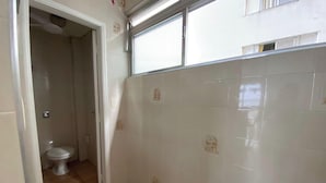 Un baño con azulejos blancos, un inodoro y una ventana con persianas.