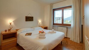 Ein Hotelzimmer mit einem großen Bett, zwei Nachttischen, einem Fenster mit Vorhängen, einem Heizkörper und einem Wandbild.