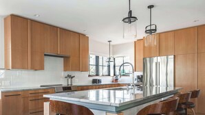 A modern kitchen with wooden cabinets, a large island with bar stools, stainless steel appliances, and pendant lighting. - Stay at Old Garden Beach (Rockport)