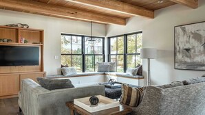 A living room with a wooden ceiling, built-in shelves, a flat-screen TV, a corner seating area with a view, and a large abstract painting. - Stay at Old Garden Beach (Rockport)