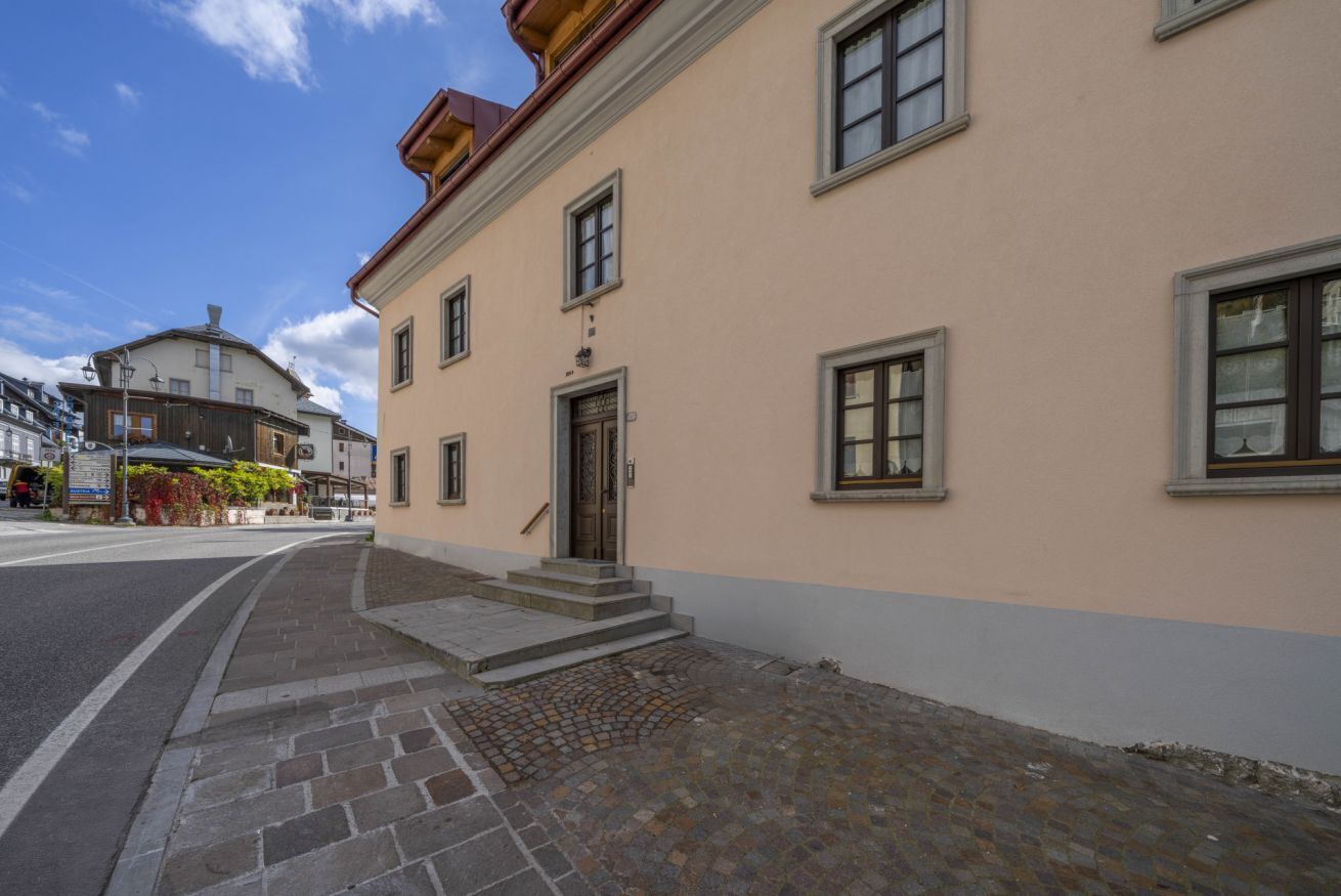 Ein Gebäude mit beiger Fassade, Stufen, die zu einer Tür führen, und ein gepflasterter Bürgersteig.