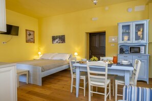 Ein Zimmer mit einem Bett, einem Esstisch mit Stühlen, einer Mikrowelle und einem Schrank mit Glastüren.