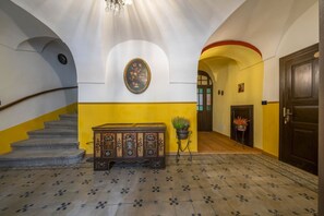 Una scala con ringhiera in legno, una panca decorata con motivi floreali, un quadro appeso al muro e una pianta in vaso.