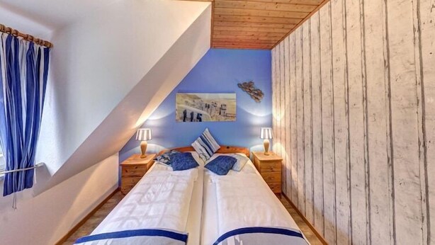 Une chambre avec deux lits, un plafond en bois, des murs bleus et un tableau accroché au mur.
