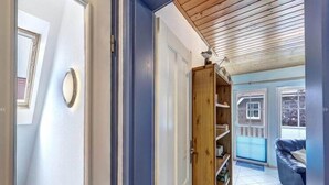 Un couloir avec une porte en bois, une bibliothèque intégrée et une vue sur une pièce bleue, avec une fenêtre et un canapé en cuir noir.