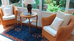 Una habitación acogedora con muebles de mimbre, una mesa redonda con lámpara y vistas a zonas verdes a través de amplios ventanales.