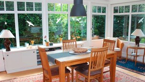 Un comedor con mesa y sillas de madera, un tapete estampado y ventanas amplias con vista a zonas verdes.