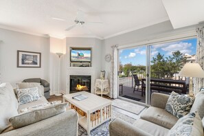 A living room with a fireplace, a television, and a balcony with outdoor furniture. - Lorelei I 108 by Seaside Vacations & Sales (Ocean City)