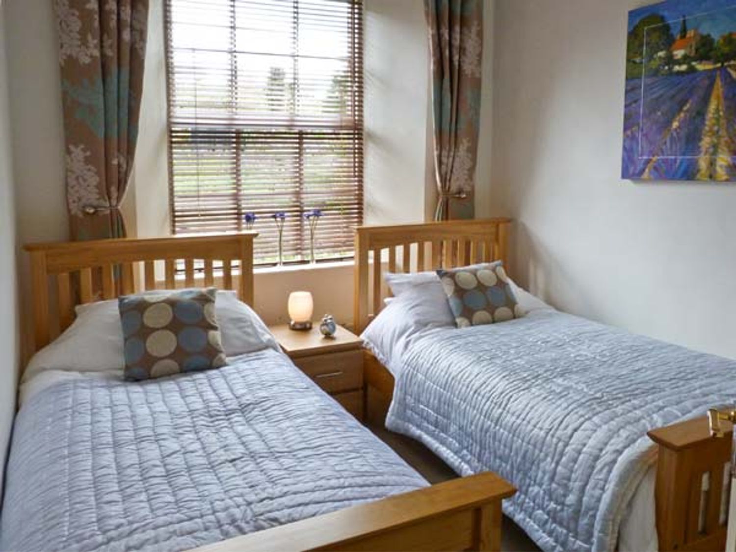 A bedroom with two single beds, wooden headboards, and a nightstand with a lamp.