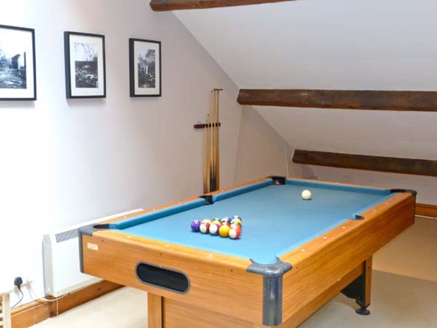 A pool table with balls in a room with white walls and framed pictures.