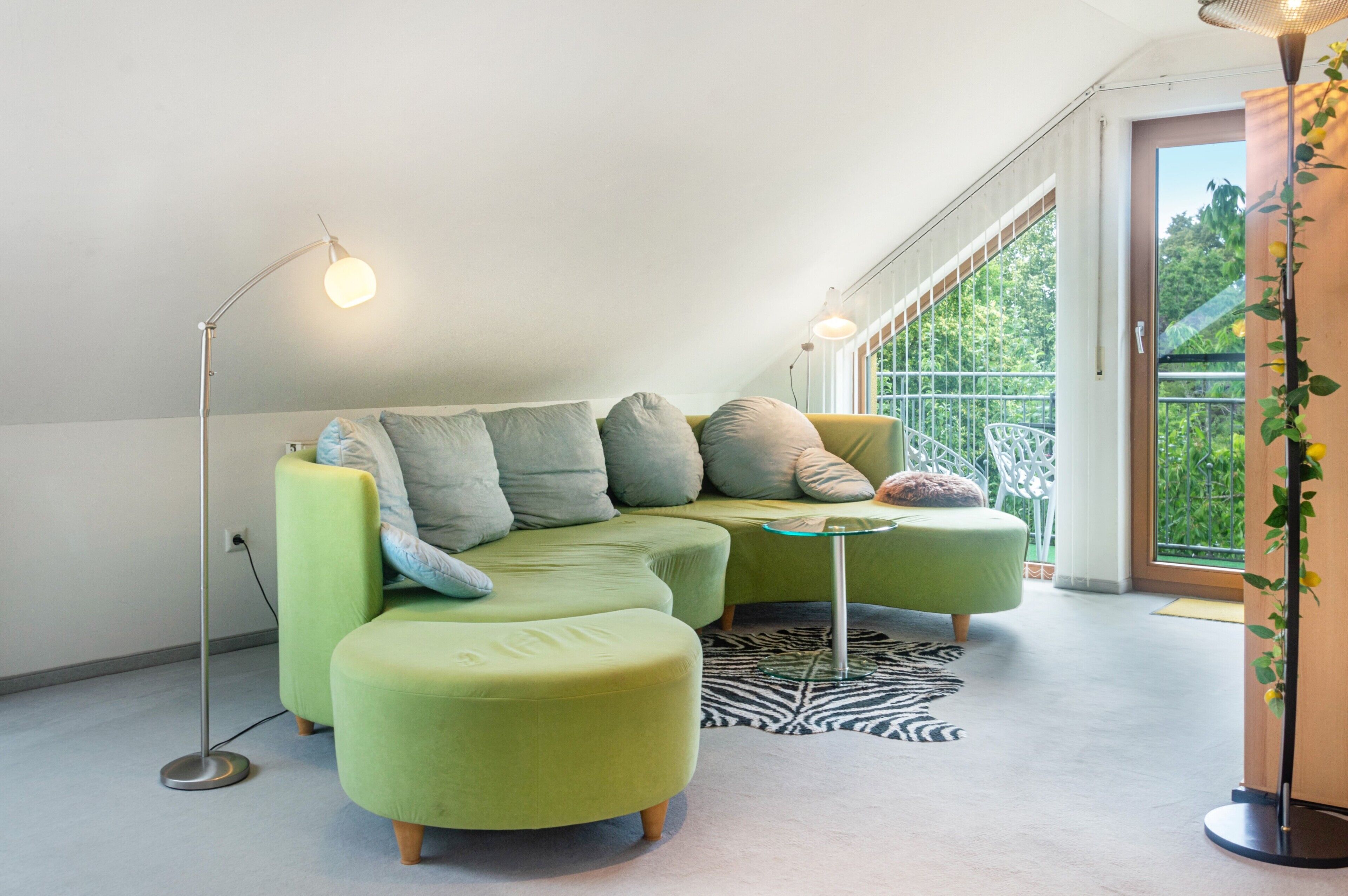 Ein modernes Wohnzimmer mit einem grünen Ecksofa, einem kleinen runden Tisch und einem Zebra-Teppich.