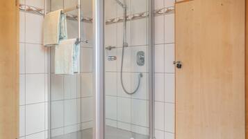 Une douche fermée par des parois en verre, dotée d’un pommeau de douche à main, d’un porte-serviettes et d’une porte en bois.