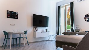 A modern hotel room with a bed, a TV mounted on the wall, a dining table with chairs, and a window with curtains. - Notes in Corvetto by Wonderful Italy (Genoa)