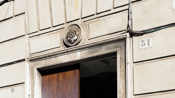 A building entrance with a wooden door, a number plaque, and a utility pipe. - Notes in Corvetto by Wonderful Italy (Genoa)