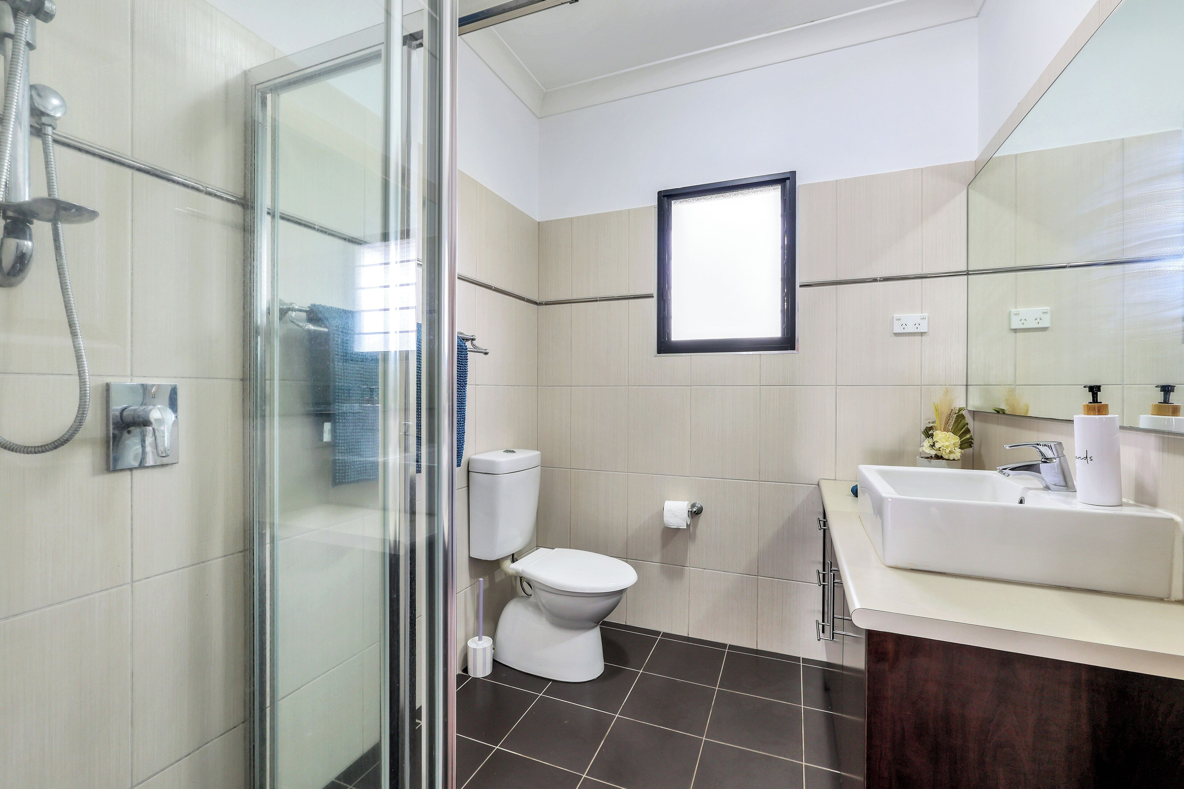 A modern bathroom with a glass shower enclosure, a white toilet, and a sink with a mirror above it.