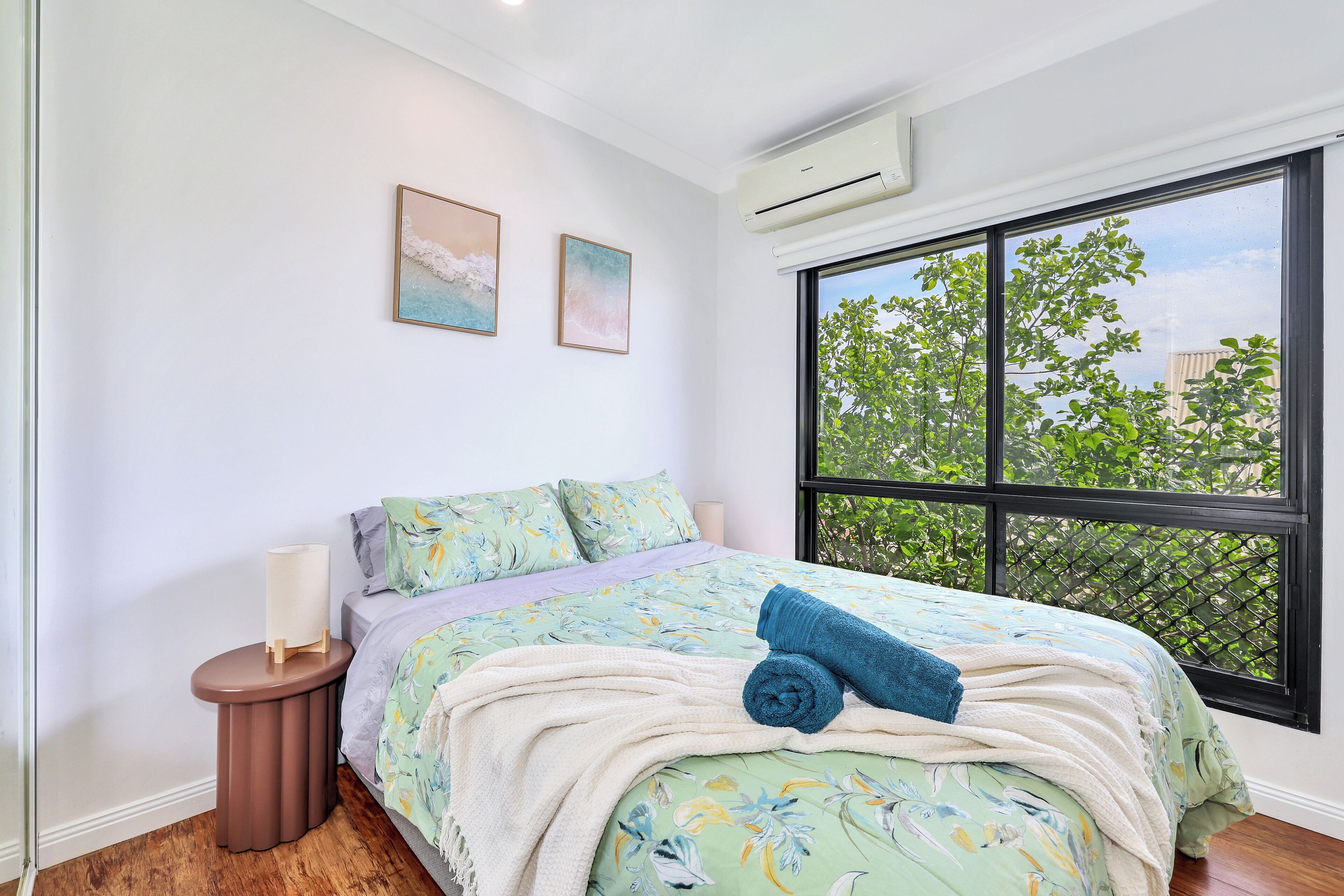 A bedroom with a bed, a nightstand, a window, and two wall-mounted artworks.