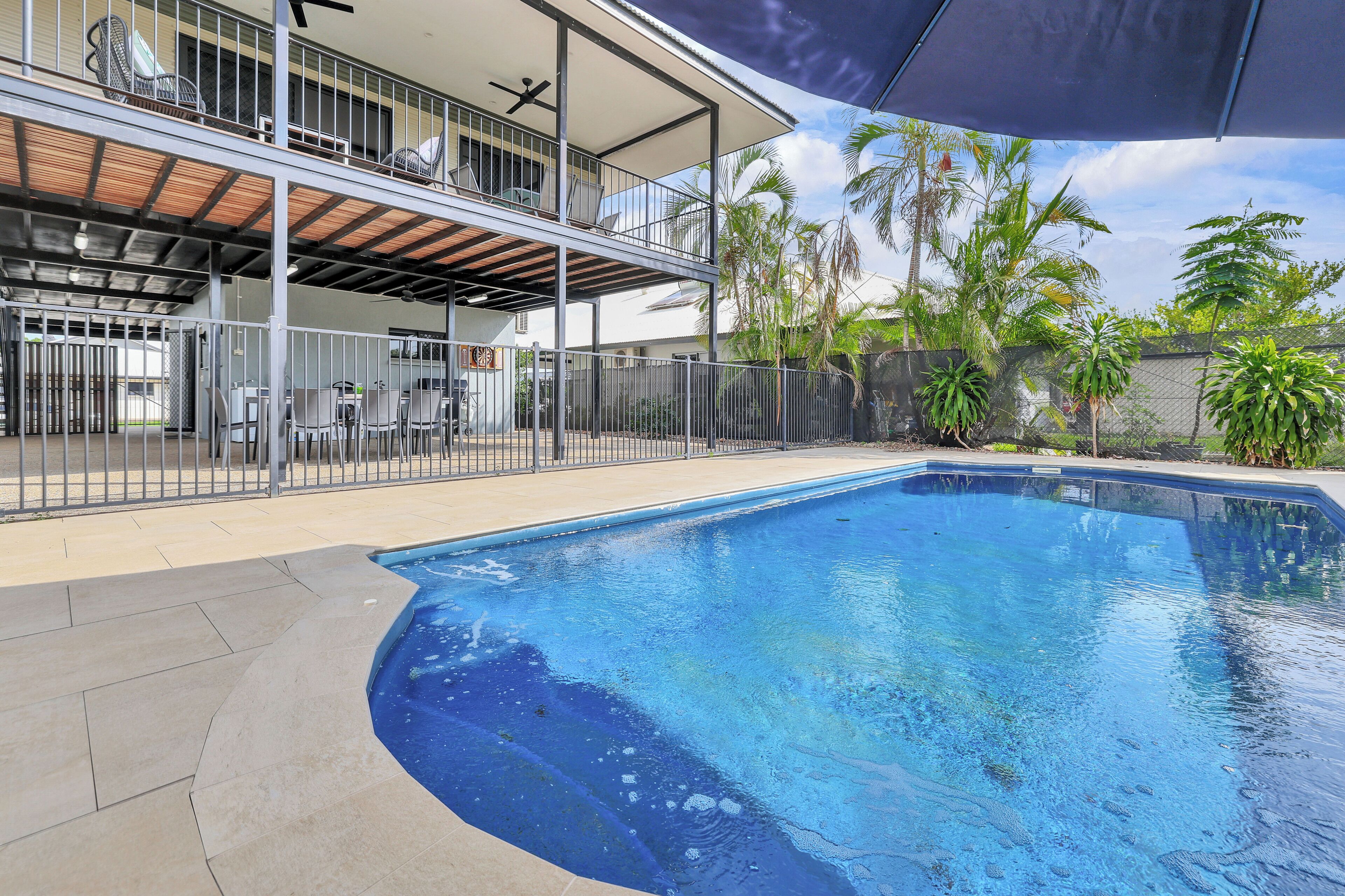 Ein Schwimmbecken mit überdachter Terrasse, umzäunter Deck und umliegenden Palmen.