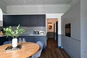 A modern kitchen with dark cabinets, a central island, and a dining area with a wooden table and chairs. - Luxury 2.5 Bedroom Flat in Southsea (Portsmouth)