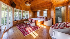 A cozy log cabin with a large bed, a seating area, and a view of the outdoors through large windows. - Ferma Gold | Double Room by PikHost (Tiranë)